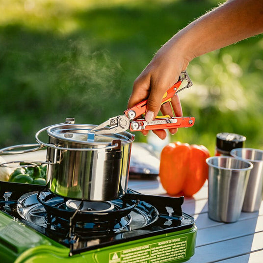 A person cooks on a stove, using Leatherman Signal to handle a pot filled with food.