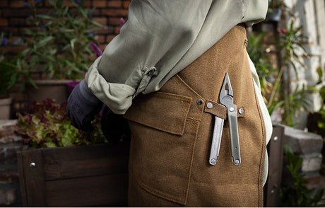 A stainless steel Leatherman Bond hanging on the side of a Gardening apron with pliers showing.