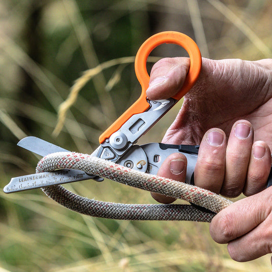 A man using an orange and black Leatherman Raptor Rescue shears to cut a thick rope.