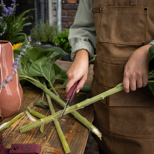 Woman using the knife on a Heathered Cranberry Leatherman Bond to cut the bottom of a sunflower stem.