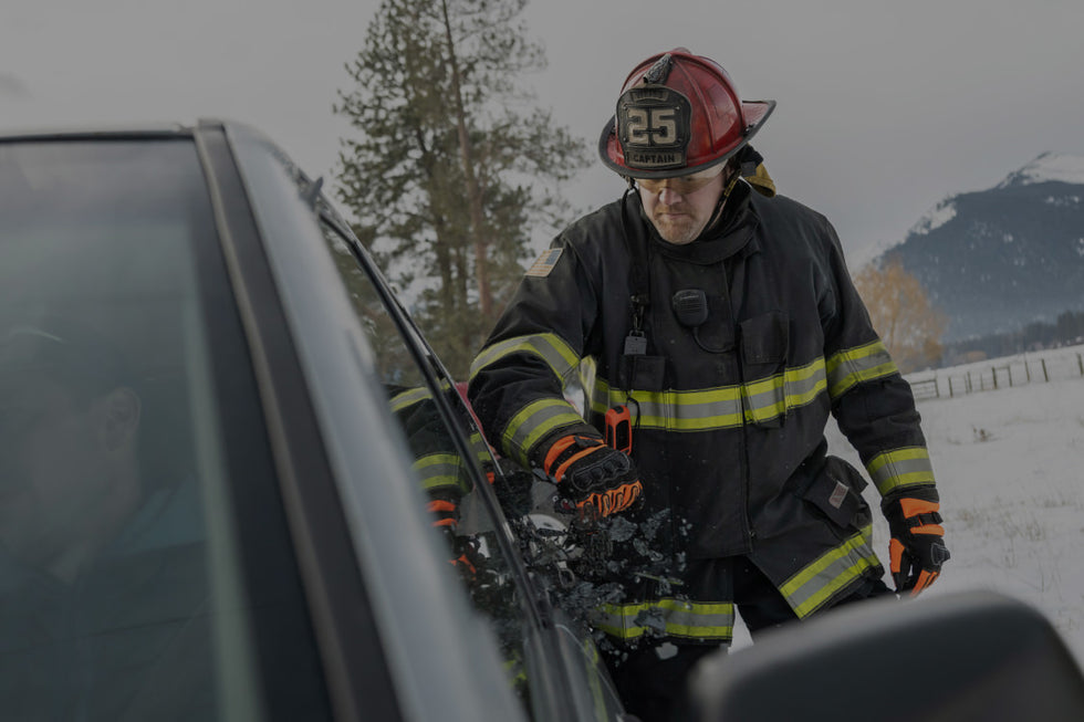 A firefighter stands beside a car, wearing protective gear and looking ready for action.